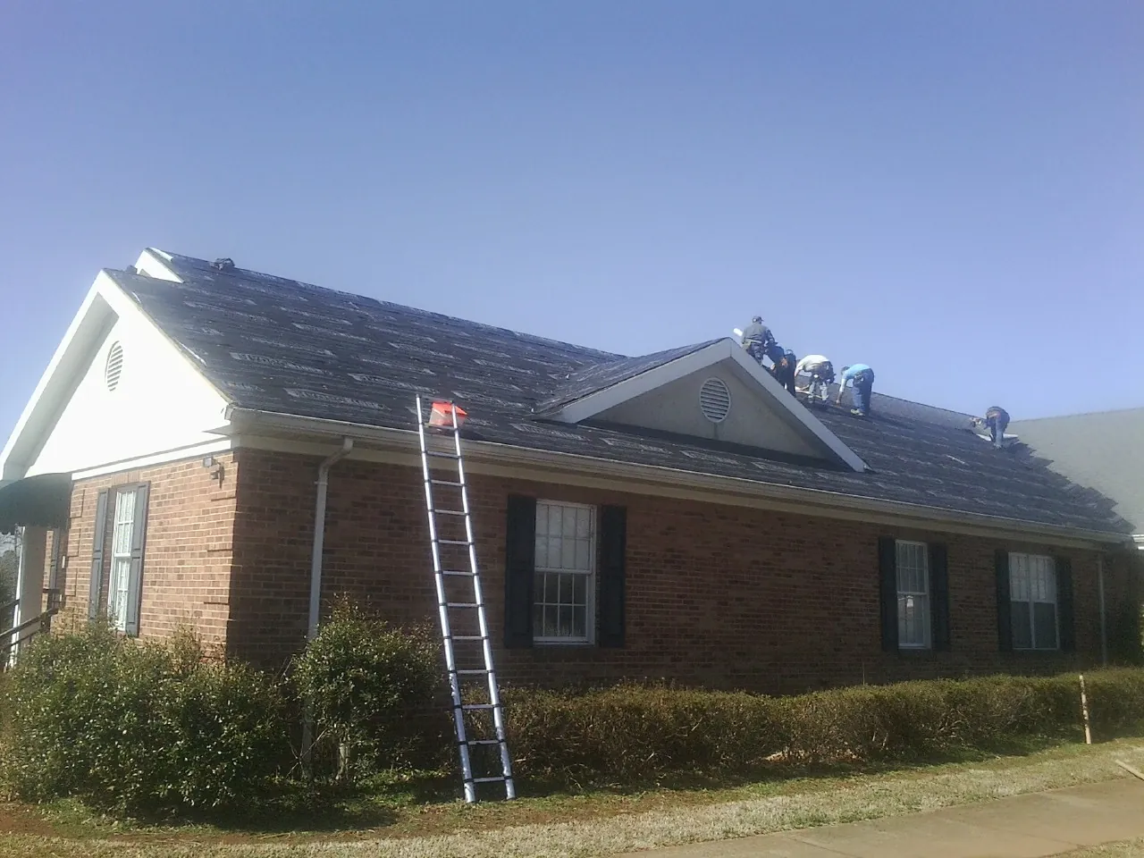 Crew tearing shingles off a brick ranch roof with a ladder set — Metal Roof Repair work by our crew in Orford
