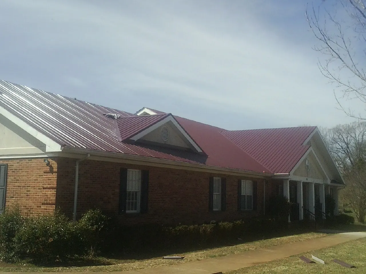 Red metal roof with gabled entries on a long brick building, from a Hail Damage Roof Repair job in Orford