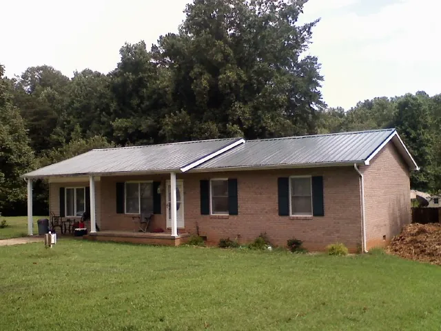 Gray metal roof on a brick ranch house with a side carport in Orford
