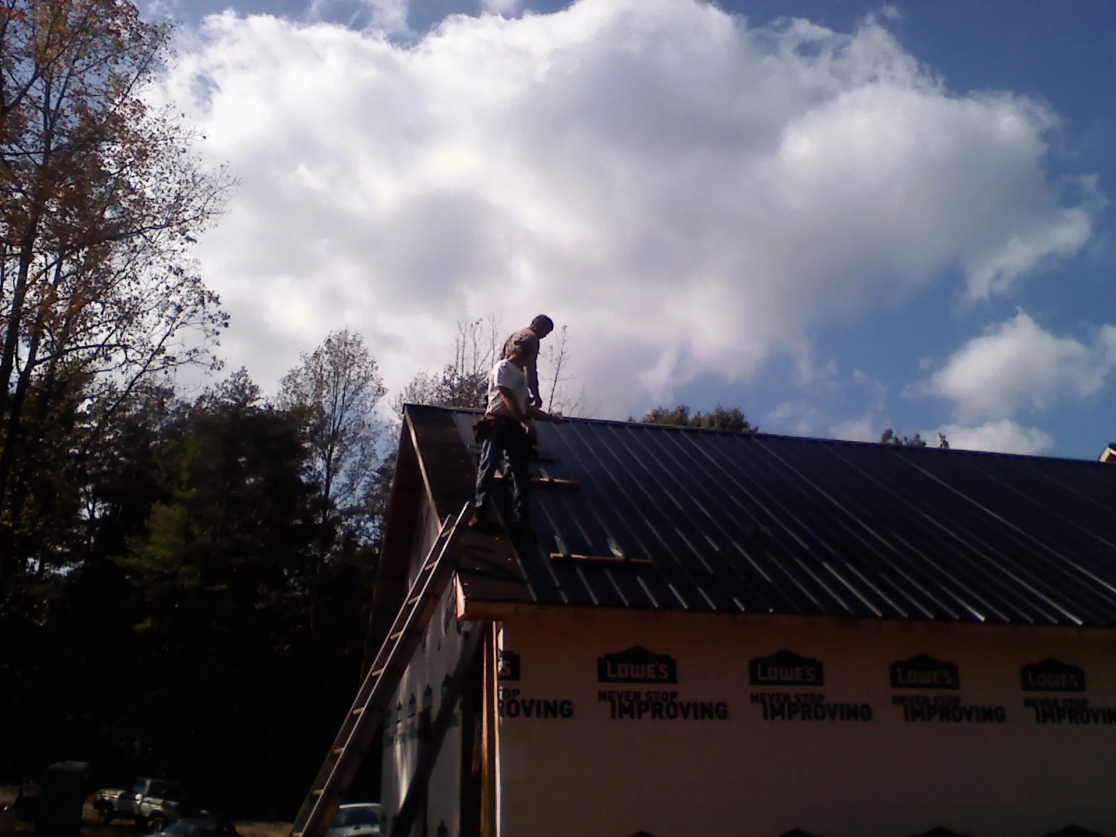 Roofer fastening dark metal panels high against a cloudy sky, from a Roof Inspection job in Orford