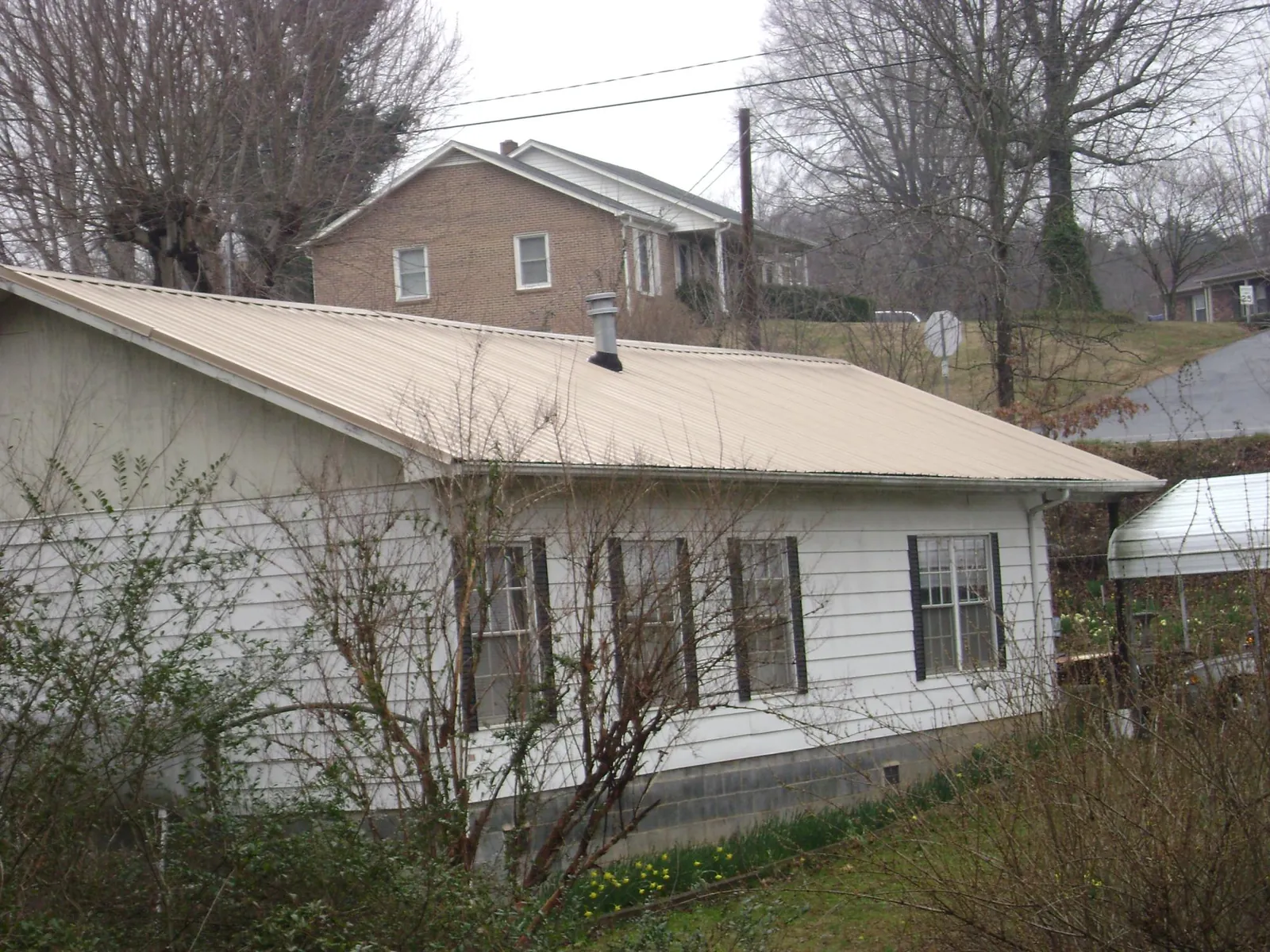 Tan metal roof on a white sided house set into a hillside — Commercial Roofing by Roofing Brothers in Orford