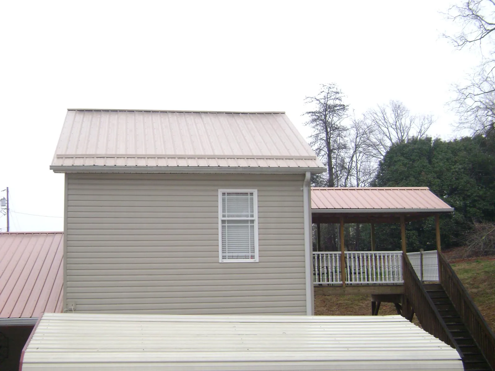 Tan metal roofs on a two story addition and attached porch, from a Roof Replacement job in Orford